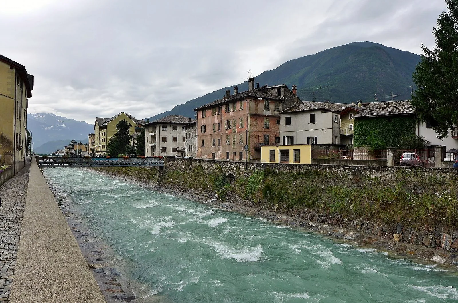 Il fiume Adda che scorre tra gli argini in pietra a Tirano, con le case e le montagne della Valtellina sullo sfondo